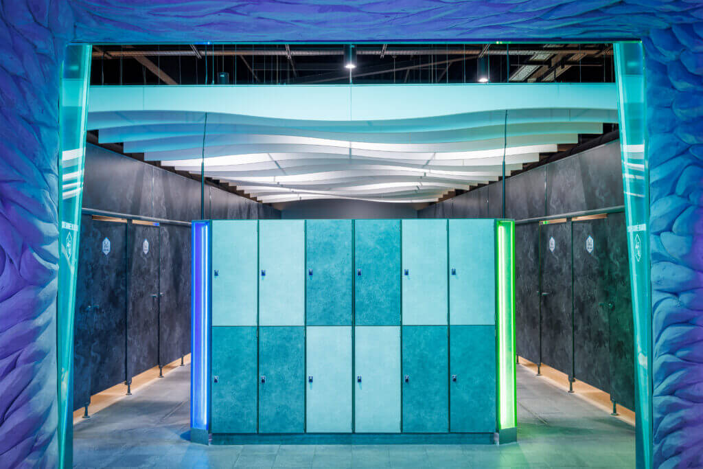 Îlot de casiers bleu-vert en stratifié compact, encadré de colonnes lumineuses, dans les vestiaires de l’Aquascope
