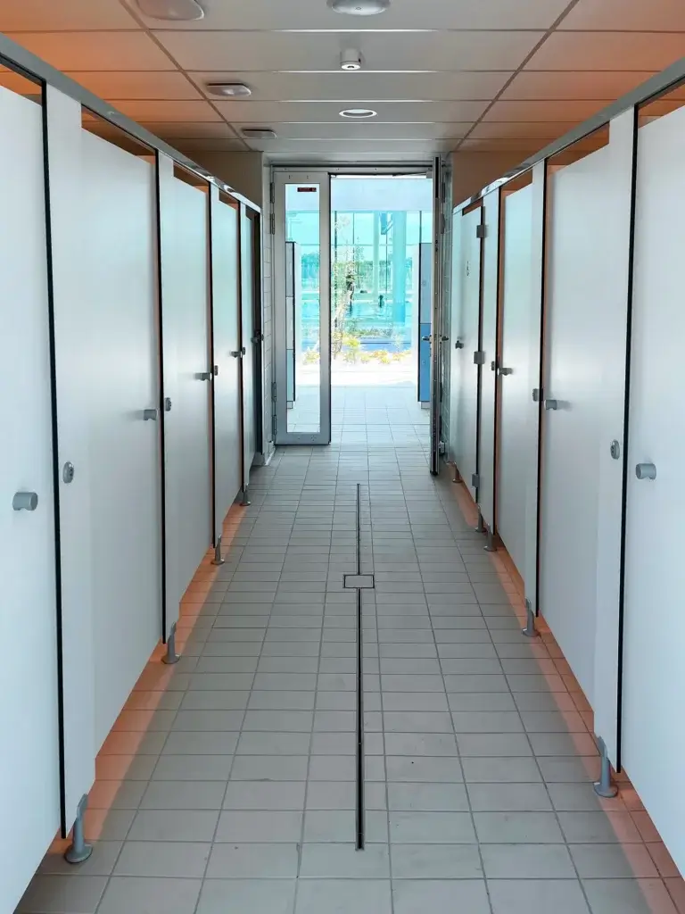 Allée de cabines blanches en stratifié compact, montées sur pieds, ouvrant sur le bassin extérieur du centre aquatique de Valognes