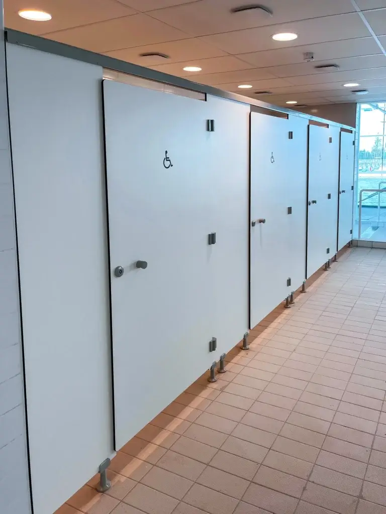 Quatre cabines blanches en stratifié compact signalées par le pictogramme d'accessibilité, montées sur pieds