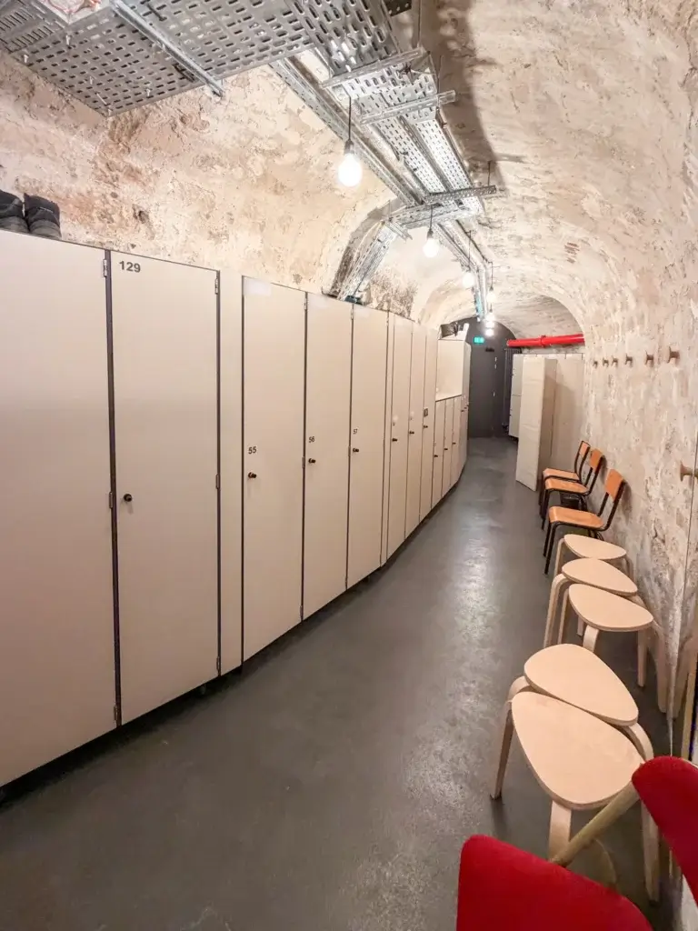 Casiers de change à une porte alignés le long d'une galerie voûtée en pierre, face à des chaises et des tabourets