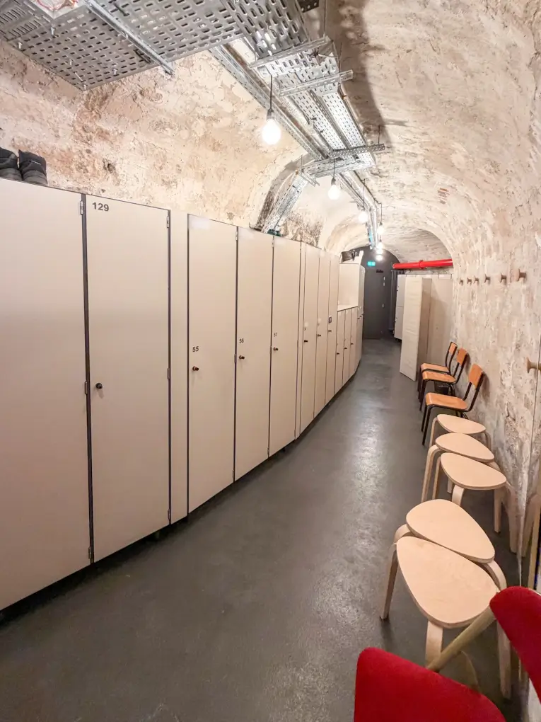 Casiers de change à une porte alignés le long d'une galerie voûtée en pierre, face à des chaises et des tabourets
